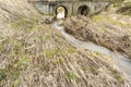 Spring flow of water in the bed of a small river passes through the large drainage pipes under the bulk bridge Royalty Free Stock Photo