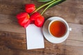 Spring flowers. Bouquet of Red tulips with tea cup and present card on brown wooden background. Mother`s Day and