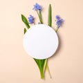 Spring flowers and rounded white blank paper on pastel beige background. Tender creative layout. Spring nature concept. Flat lay