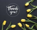 Spring flowers. `Thank you!` written in calligraphic style. Frame made of yellow tulip flowers on black background. Flat lay, to Royalty Free Stock Photo