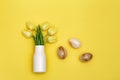 Spring flowers of tulip in white vase and decorative Easter eggs made from natural gemstone onyx on yellow backdrop. Royalty Free Stock Photo