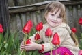 Spring in the garden of a beautiful little girl sitting near tulips.