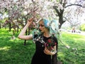 Spring girl with green hair stands under blooming cherry tree, which blooms