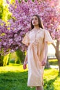 Spring girl. Hanami celebration in sakura blooming garden. Beautiful young stylish woman walking in sakura park and