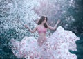 Spring girl with wavy hair dancing dancing on a background of flowering trees. She wears a pink dress with flowers that Royalty Free Stock Photo