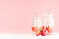 Spring healthy milk beverages with cut ripe strawberry, red striped straws on gentle pastel pink background, white wood table.