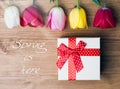 Spring is here. Gift box and tulips on wooden background