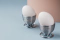 Spring holiday Easter concept. Two fresh white chicken eggs in metal stands on a double pink and blue background. Farm home Royalty Free Stock Photo