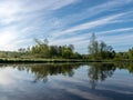 Spring landscape with a beautiful calm river, green trees and grass on the river bank, peaceful reflection in the river water