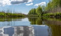 Spring landscape with a beautiful calm river, green trees and grass on the river bank, peaceful reflection in the river water