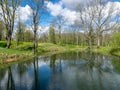 Spring landscape with tree silhouettes, green grass and a small pond, reflections of clouds and trees in the water Royalty Free Stock Photo