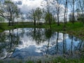 Spring landscape with tree silhouettes, green grass and a small pond, reflections of clouds and trees in the water Royalty Free Stock Photo