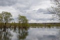 Spring landscape with trees, new foliage, grass, river in flood, reflection in the water, a village in the distance Royalty Free Stock Photo