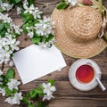 Spring layout with branches of a flowering apple tree, a cup of tea and a straw hat Royalty Free Stock Photo