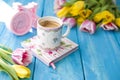 Spring morning, fragrant coffee and tulips of yellow and pink color. Donuttsy copies. Blue wooden background, pink alarm clock and Royalty Free Stock Photo