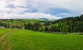 Spring mountains scene with wooden split rail fence across a green and lush pasture, a country road and old houses on the valley Royalty Free Stock Photo