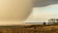 Spring natural and urban panoramic landscape with approaching huge storm cloud and heavy rain over burnt field and large city on