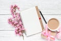 Spring pink blossoming flowers with blank paper notepad, macarons, coffee cup and gift box on white wooden table