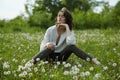 Spring portrait of a girl sitting in a field on the grass among dandelion flowers. Cheerful girl enjoys Sunny spring weather. Royalty Free Stock Photo