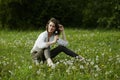 Spring portrait of a girl sitting in a field on the grass among dandelion flowers. Cheerful girl enjoys Sunny spring weather. Royalty Free Stock Photo