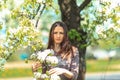 Spring portrait. Young beautiful white girl in a brown sports suit stands near blossoming branches of apple trees in the garden.