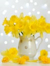 Spring postcard. Bouquet of yellow daffodils in a jug on table against the background of glowing lights. Spring composition.