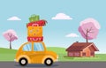 Spring road trip on small retro yellow car with colorful suitcases on the roof. Spring landscape with blooming trees and a wooden