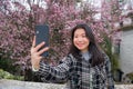 Spring sakura selfie - young happy and cute Asian Chinese tourist woman taking self portrait with mobile phone smiling cheerful in Royalty Free Stock Photo