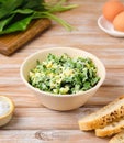 Spring salad of wild garlic and boiled eggs in a ceramic bowl on a wooden background. The use of wild plants for food, the first Royalty Free Stock Photo