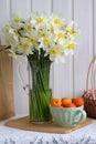 Spring still life with a bouquet of white daffodils in a glass jug and a bowl of apricots Royalty Free Stock Photo