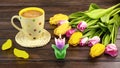 Spring still life with a white polka dot cup of coffee, a bouquet of yellow and pink tulip flowers and a candl