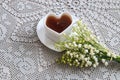 Spring tea party: a mug of tea in the shape of a heart, a bouquet of lilies of the valley on a gray openwork napkin, top view