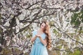 Spring touch. Happy beautiful young smiling woman in blue dress enjoy fresh flowers and sun light in blossom park at
