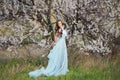 Spring touch. Happy beautiful young woman in blue dress enjoy fresh flowers and sun light in blossom park at sunset.