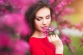 Spring touch. Happy beautiful young woman in red dress enjoy fresh pink flowers and sun light in blossom park at sunset.