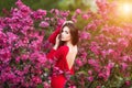 Spring touch. Happy beautiful young woman in red dress enjoy fresh pink flowers and sun light in blossom park at sunset. Royalty Free Stock Photo