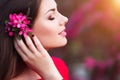 Spring touch. Happy beautiful young woman in red dress enjoy fresh pink flowers and sun light in blossom park at sunset.