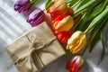 Spring tulips lying on table with wrapped gift box. Royalty Free Stock Photo