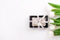 Spring website header template. White tulip black gift box with silver ribbon on light background flat lay. Copy space