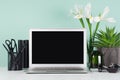 Spring workplace with blank notebook screen, black stationery, books, candlestick, white fresh flowers, aloe in elegant green mint