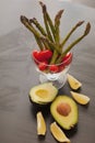 spring young asparagus, cherry tomatoes and ripe avocado in a composition in a glass vase on a black wooden background.