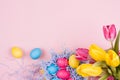 Springtime easter festive background - homemade painted multicolored eggs, tulips bouquet on pastel light pink background.