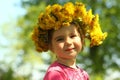 Springtime sunlit portrait of a cute two years old girl posing with a dandelion wreath, looking at the camera Royalty Free Stock Photo