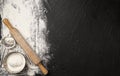 Sprinkled wheat flour and wooden rolling pin on black background