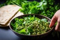 sprinkling freshly chopped coriander leaves over a falafel bowl