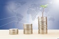 Sprout growing from stack of coins on wooden desk on blurred world map and line graph background