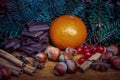 Spruce branches, tangerine, nuts, cinnamon and chocolate on wooden background.