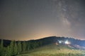 Spruce forest and lit houses at night, visible Milky Way galaxy, clear sky, long exposure