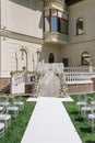 Square arch with flowers, long white walkway and chairs with glass backs on green lawn