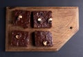 Square baked slices of brownie chocolate cake with walnuts on a brown wooden surface. Cooked homemade food